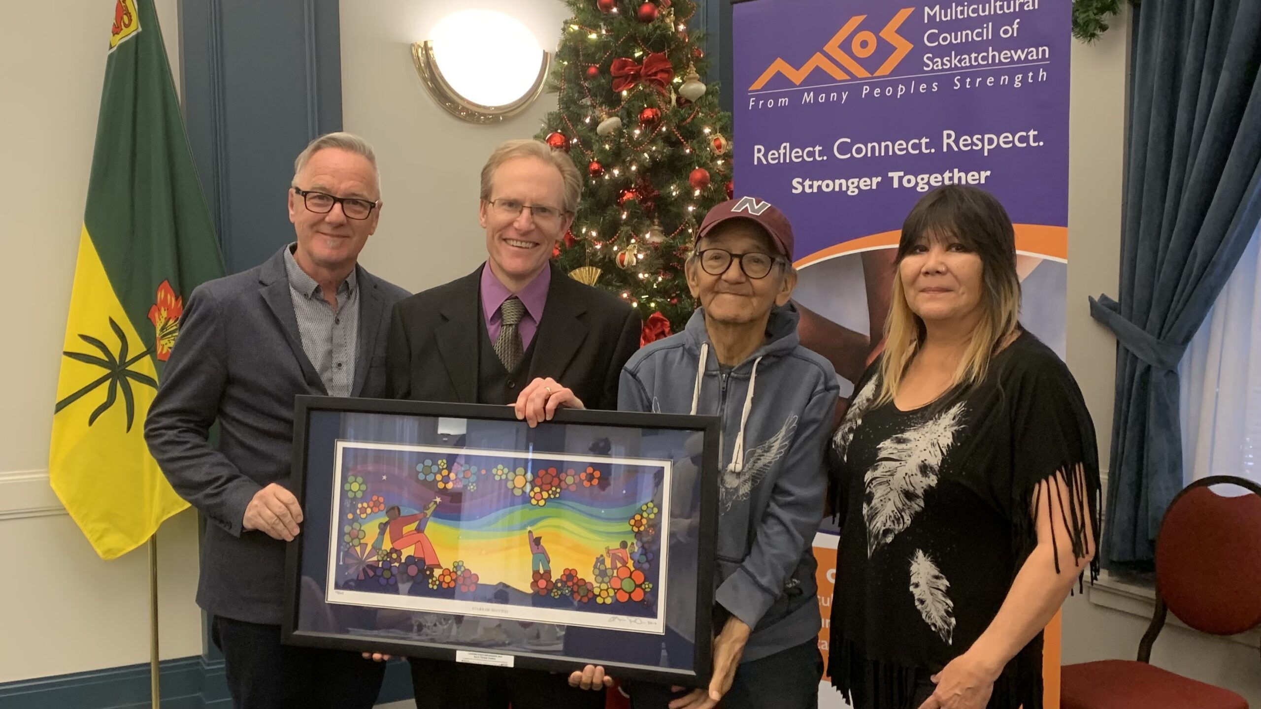 photo of We Treaty People artists Darryl Dozlaw, Stephen Waldschmidt, Erroll Kinistino, and Erroll’s partner Josie Linka, holding the painting by Kevin Peeace given with the Leading Together Award